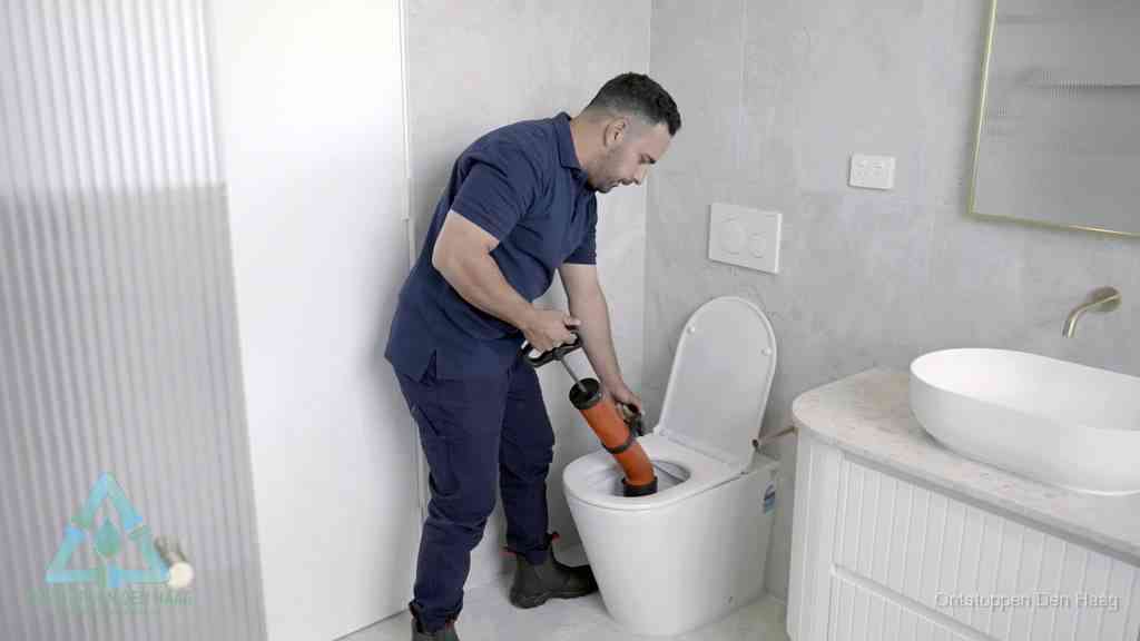 Een monteur buigt over een wandcloset en duwt met de hand een persluchtontstopper in de toiletpot om de verstopping handmatig los te maken in Den Haag