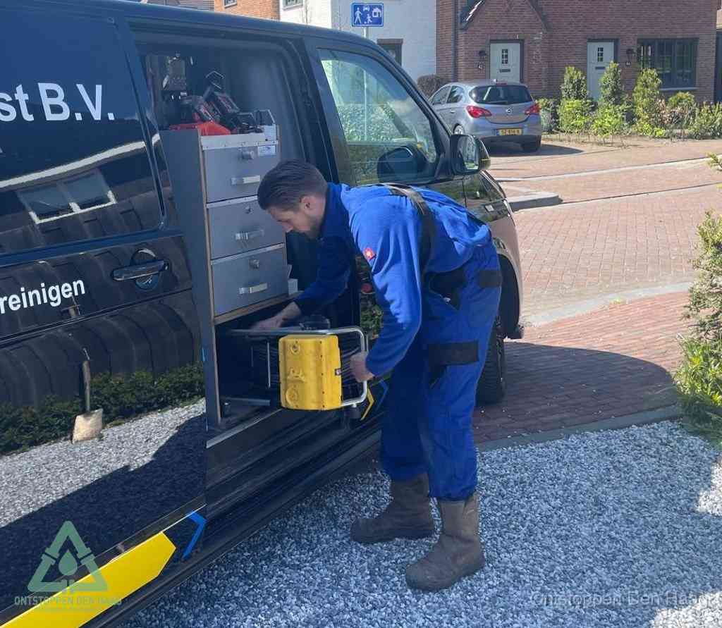 Een monteur pakt buiten op de oprit gereedschap uit de bedrijfsbus, het moment om een professional in te schakelen voor een verstopte afvoer in Den Haag