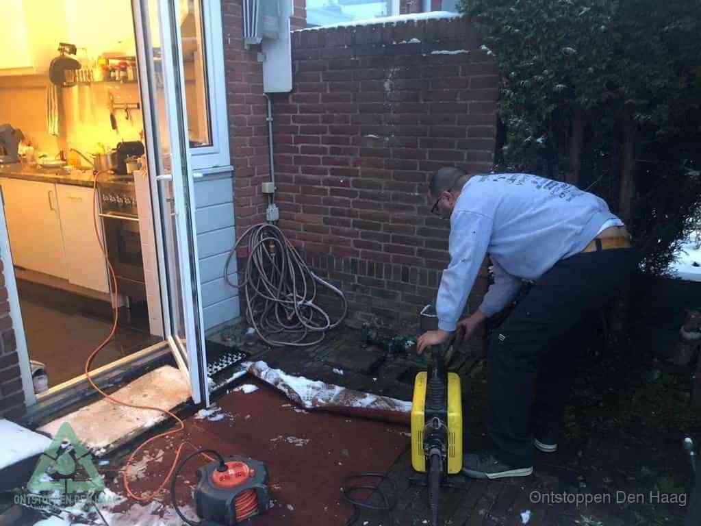 Een monteur werkt buiten bij een open riool-/grondput met een elektrische ontstoppingsmachine om een verborgen afvoerprobleem op te sporen in Den Haag