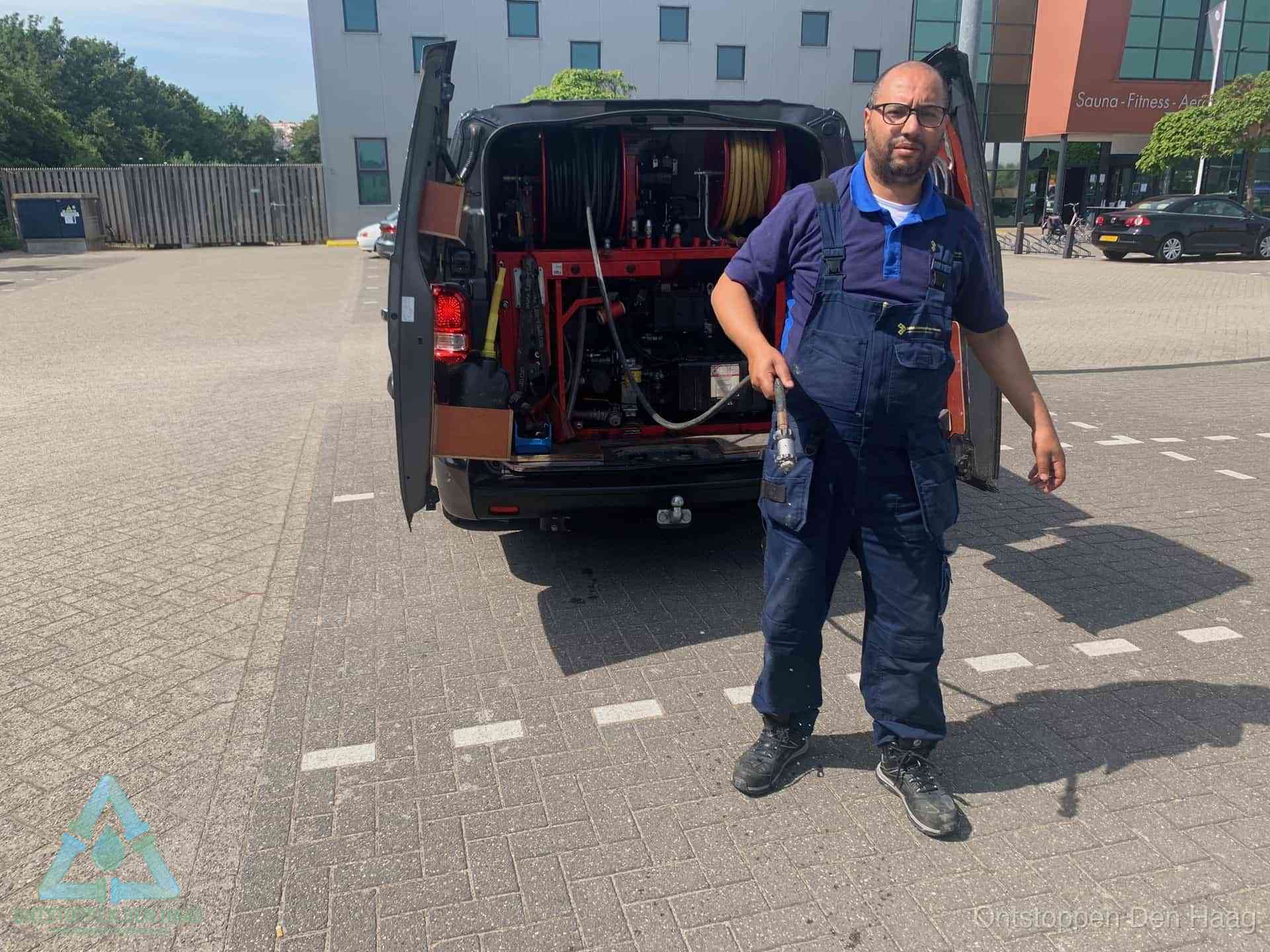 Een monteur bij zijn bestelbus met een hogedruk- en rioolreinigingsunit, klaar om de oorzaak van terugkerende wc-verstoppingen aan te pakken in Den Haag
