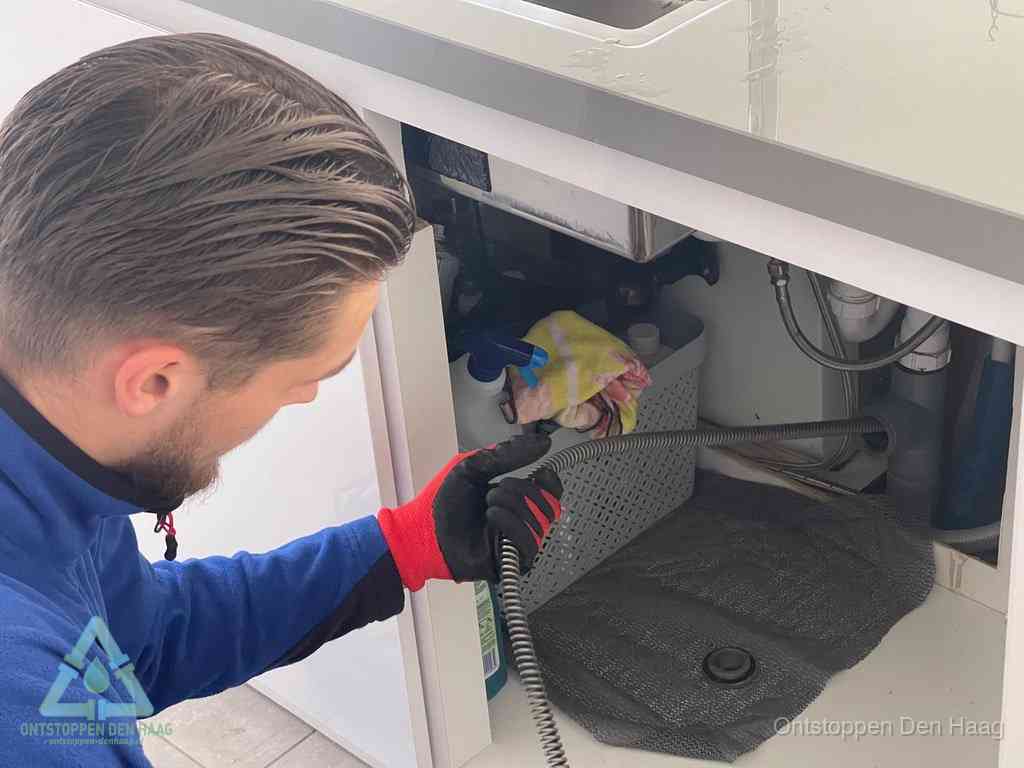 Een monteur voert een flexibele ontstoppingsveer in de afvoer om een verstopping voorbij de bocht van het toilet te bereiken in Den Haag