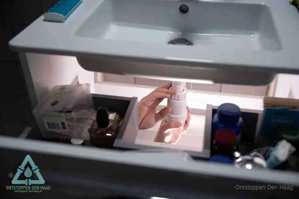 Een pompfles met zeep boven een wastafel in de toiletruimte, de warm water en afwasmiddel-methode om de wc te ontstoppen in Den Haag