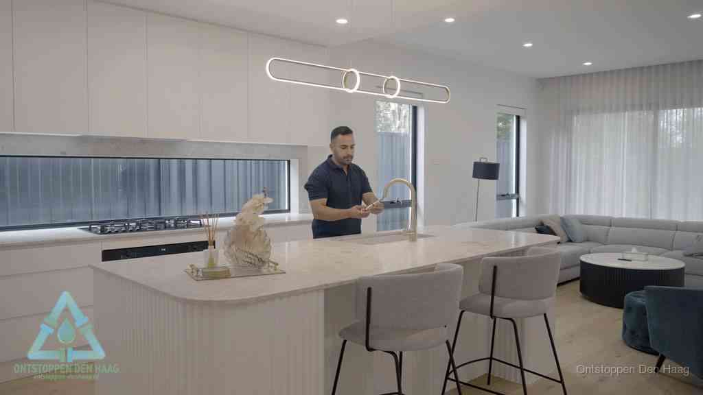 Een bewoner bij de keukenspoelbak die zelf aan de slag gaat met een verstopte gootsteen in Den Haag